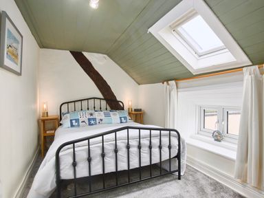 A bedroom with a black metal bed frame two bedside tables with lamps a skylight window and a framed picture on the wall at Stonewall in Sandsend