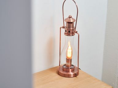 A copper lantern-style lamp with a lit bulb on a wooden surface against a white wall at Stonewall in Sandsend