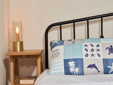 A bed with a patterned pillow and a wooden bedside table with a lamp and books at Stonewall in Sandsend