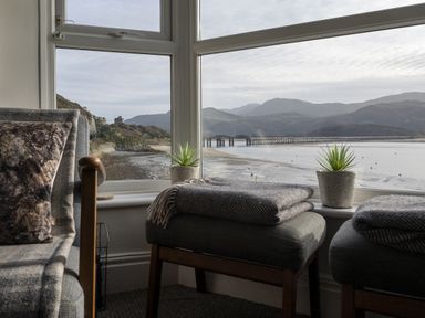 A seating area with two stools, small plants on the windowsill, and a view of a river and bridge at Harbour View - Flat 2 in Barmouth