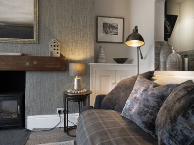 A living room corner with a plaid sofa, cushions, a lamp on nested tables, fireplace, and decorative vases at Harbour View - Flat 2 in Barmouth