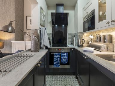A small kitchen with gray countertops blue cabinets electric stove oven sink kettle and decorative vases at Harbour View - Flat 2 in Barmouth