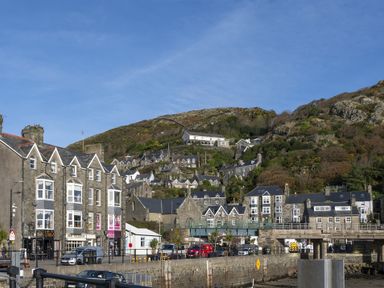 Stone buildings and hillside houses near a waterfront with a road and vehicles at Harbour View Flat 2 in Barmouth