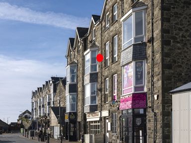 A street with stone buildings housing shops and restaurants under a blue sky at Harbour View - Flat 2 in Barmouth