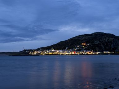 A coastal town with lights on near a hill at dusk at Harbour View - Flat 2 in Barmouth