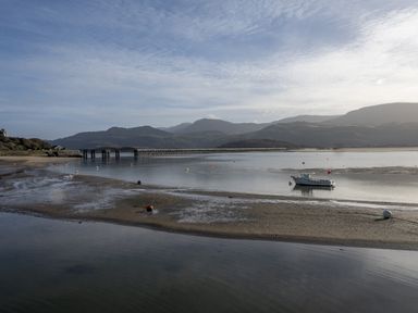 A river with a small boat and a bridge with mountains in the background at Harbour View - Flat 2 in Barmouth