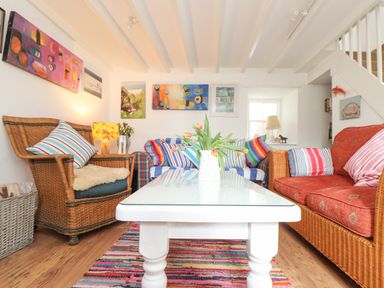 A living room with wicker armchairs sofas and a white coffee table with flowers at Rose Cottage Lower Bostraze near St Just