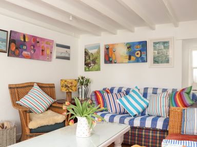 A sitting area with wicker chairs a sofa with striped cushions a white coffee table with flowers and paintings on the wall at Rose Cottage in Lower Bostraze near St Just