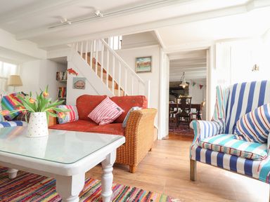 A living room with a glass coffee table a red sofa striped armchair and a staircase at Rose Cottage in Lower Bostraze near St Just