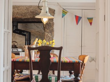 A dining area with a wooden table and chairs a striped tablecloth and a stone fireplace at Rose Cottage in Lower Bostraze near St Just