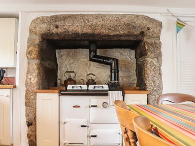 A kitchen with a vintage stove set in a stone fireplace and a wooden table with striped cloth Rose Cottage Lower Bostraze near St Just