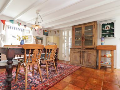A dining room with wooden chairs around a table a rug and a wooden cabinet at Rose Cottage Lower Bostraze near St Just