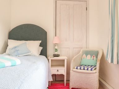 A bedroom with a bed a bedside table with lamp and a wicker chair at Rose Cottage in Lower Bostraze near St Just