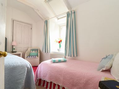 A bedroom with two single beds a chair a side table and a window with striped curtains at Rose Cottage in Lower Bostraze near St Just