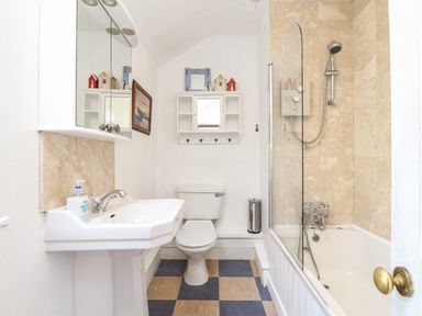 A bathroom with a sink a toilet a bathtub with shower an overhead cabinet and a wall cabinet above the toilet at Rose Cottage in Lower Bostraze near St Just