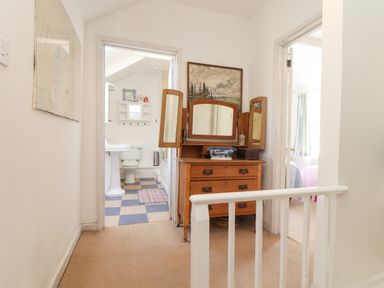 A hallway with a wooden dressing table with mirrors a bathroom with a toilet and sink and a bedroom with a bed at Rose Cottage in Lower Bostraze near St Just