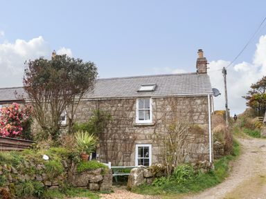Stone cottage with white window frames, plants and flowers outside and a gravel driveway at Rose Cottage in Lower Bostraze near St Just