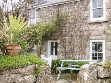 Stone exterior of a cottage with two windows a white door a green picnic table and potted plants at Rose Cottage Lower Bostraze near St Just