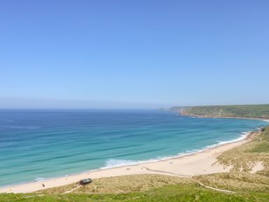 A sandy beach with people near the ocean and grassy dunes on the shore at Rose Cottage in Lower Bostraze near St Just