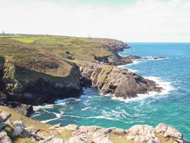 Rocky coastal cliffs with green grassy areas and blue ocean water at Rose Cottage in Lower Bostraze near St Just