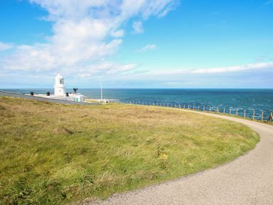 A lighthouse near the ocean with a curved road and grassy land at Rose Cottage in Lower Bostraze near St Just