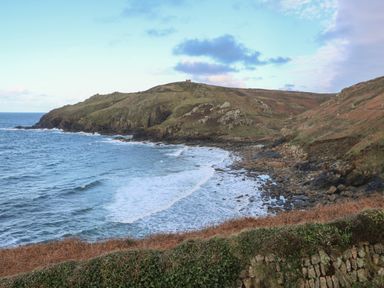 A coastal landscape with rocky cliffs and waves crashing on the shore at Rose Cottage in Lower Bostraze near St Just