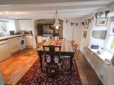 A kitchen with a striped tablecloth on a dining table and wooden chairs at Rose Cottage in Lower Bostraze near St Just