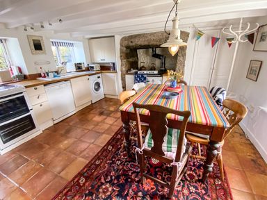 A kitchen with a striped tablecloth on a dining table surrounded by chairs and a patterned rug on the floor at Rose Cottage in Lower Bostraze near St Just