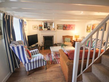 A living room with striped curtains and armchairs near a fireplace in Rose Cottage Lower Bostraze near St Just