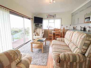 A living room with patterned sofas a wooden coffee table a dining table with chairs and a wall-mounted television at Morlyn Guest House Apartment in Llandanwg near Harlech