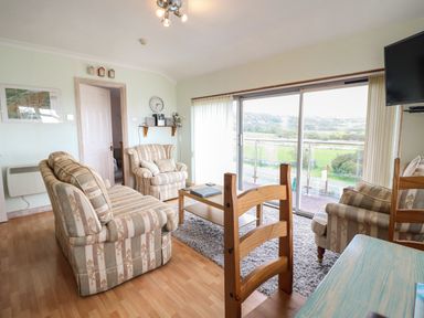 A living room with sofas a coffee table a wall clock and a sliding glass door at Morlyn Guest House Apartment Llandanwg near Harlech