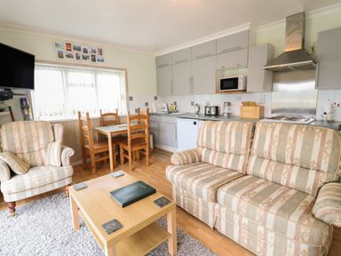 A living room and kitchen area with a sofa armchair wooden dining table and chairs and kitchen cabinets at Morlyn Guest House Apartment in Llandanwg near Harlech