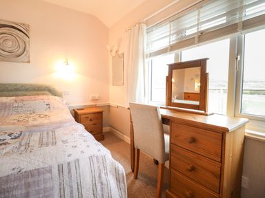 A bedroom with a bed a wooden nightstand a wooden dresser with mirror and a chair at Morlyn Guest House Apartment in Llandanwg near Harlech