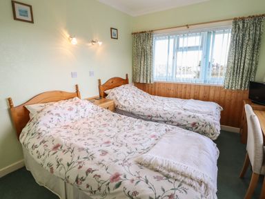 A bedroom with two single beds with floral bedding a window with curtains and a desk with a chair at Morlyn Guest House Apartment Llandanwg near Harlech