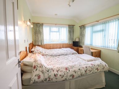 A bedroom with two single beds with floral bedding a wooden desk a chair and windows with blinds and curtains at Morlyn Guest House Apartment in Llandanwg near Harlech