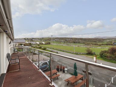 A balcony with benches and a glass railing overlooking a road and green fields at Morlyn Guest House Apartment in Llandanwg near Harlech