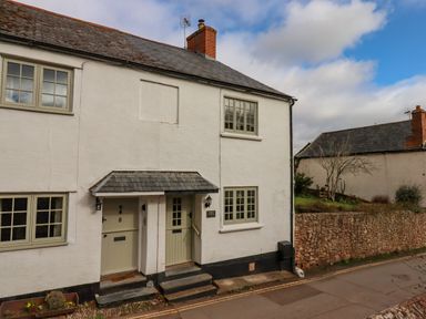 A white cottage with two green doors and windows next to a stone wall at Bodkin Cottage in Dunster