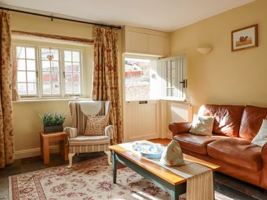 A living room with a striped armchair and brown leather sofa near a half-glazed door at Bodkin Cottage in Dunster