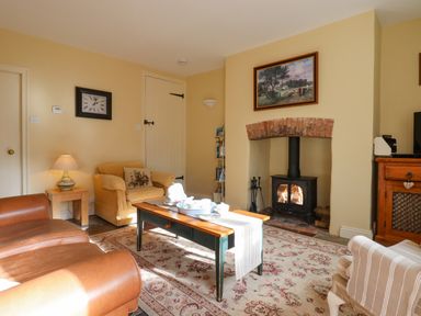 A living room with a wood burning stove coffee table armchairs and a rug at Bodkin Cottage in Dunster
