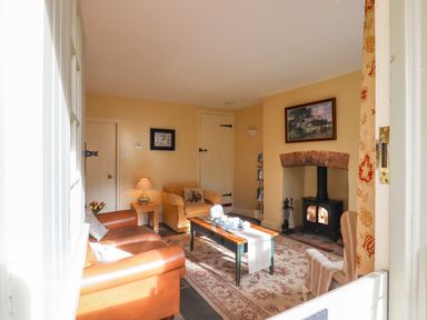 A living room with a leather sofa a beige armchair a coffee table with tea set a fireplace and a wall clock at Bodkin Cottage in Dunster