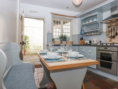A kitchen with a dining table set with bowls and wine glasses and a bench seat at Bodkin Cottage in Dunster