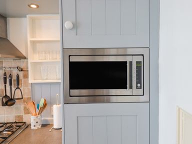 A kitchen area with a built-in stainless steel microwave in gray cabinets and utensils hanging near a gas stove at Bodkin Cottage in Dunster