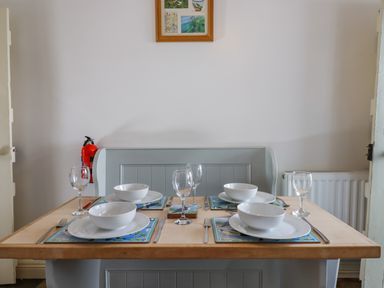 A dining table set with bowls plates glasses and cutlery in a room with a bench and fire extinguisher at Bodkin Cottage in Dunster