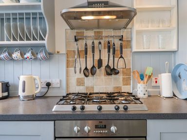 A kitchen countertop with a gas stove and hanging cooking utensils at Bodkin Cottage in Dunster