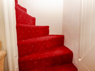 A narrow staircase with red carpet and white walls at Bodkin Cottage in Dunster