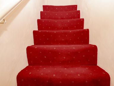 A staircase with red carpet and light-colored walls at Bodkin Cottage in Dunster