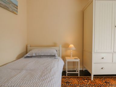 A bedroom with a single bed with striped bedding a white bedside table with a lamp and a white wardrobe on a patterned rug at Bodkin Cottage in Dunster