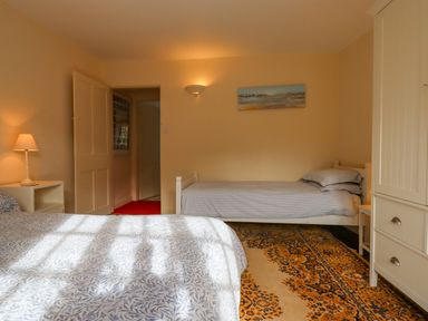A bedroom with two single beds a patterned rug a bedside table with a lamp and a white wardrobe at Bodkin Cottage in Dunster