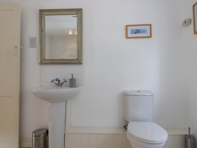 A bathroom with a white sink mirror soap dispenser and a toilet at Bodkin Cottage in Dunster