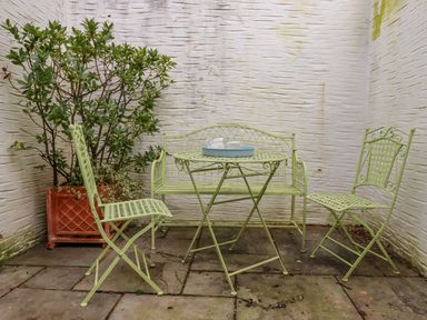 A small outdoor patio with green metal table and chairs and a potted plant against white textured walls at Bodkin Cottage in Dunster